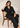 Seated model wearing the black Waist Tie-up Shirt Top with black trousers, showing the front waist tie and notched collar.